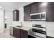 A modern kitchen featuring stainless steel appliances, dark wood cabinets, and quartz countertops with white backsplash at 17057 W Seldon Ln, Waddell, AZ 85355