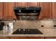 Close up of a black electric cooktop on granite counters with warm wood cabinets and dark range hood at 15558 W Big Sky Dr, Surprise, AZ 85374