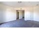 A spacious carpeted room featuring a hallway, an open door to a bathroom, and a white entry door at 3434 E Baseline Rd # 213, Phoenix, AZ 85042