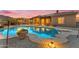 Stunning backyard at dusk featuring a large pool, covered patio, desert landscaping, and illuminated ambiance at 10931 S Santa Columbia Dr, Goodyear, AZ 85338