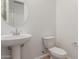 A well-lit powder room featuring a pedestal sink, a modern toilet and a round mirror at 25215 N 131St Dr, Peoria, AZ 85383