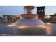 A large, tiered water fountain with lighting sits in front of a stone tower and pergola at dusk at 11128 E Segura Ave, Mesa, AZ 85212