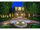 Night view of the front exterior featuring a stone facade, fountain, manicured landscaping, and illuminated trees at 9547 N 55Th St, Paradise Valley, AZ 85253