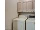Well-lit laundry area with white washer and dryer, and convenient overhead storage cabinets at 11772 E Clinton St, Scottsdale, AZ 85259