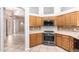 Corner kitchen featuring stainless steel appliances, wood cabinetry, tile backsplash, and tile flooring at 14130 W Bent Tree Cir, Litchfield Park, AZ 85340