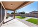 Landscaped backyard featuring artificial grass, a covered patio, block fencing, and mature trees under a sunny sky at 10449 E Lomita Ave, Mesa, AZ 85209