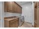 Laundry room with travertine tile flooring, wood cabinets, and modern washer and dryer at 8320 E Arroyo Hondo Rd, Scottsdale, AZ 85266