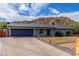 Single-story home featuring a two-car garage, desert landscaping, and a mountain in the background under a cloudy, blue sky at 9005 E Grandview Dr, Mesa, AZ 85207