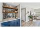 Stylish wet bar with blue cabinetry, marble countertop, brick accent wall, shelving and nearby living area at 19240 N 90Th Pl, Scottsdale, AZ 85255