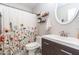 A well-lit bathroom with a modern vanity, decorative shelves, and a stylish floral shower curtain at 2323 E Aire Libre Ave, Phoenix, AZ 85022