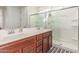 Bathroom featuring dual sinks, wood cabinets, a framed mirror and glass-door shower at 25610 N 144Th Ln, Surprise, AZ 85387