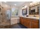 Bright bathroom with double sinks, wooden cabinets, and tiled shower and tub at 122 W Raven Dr, Chandler, AZ 85286