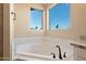 A luxurious bathroom with marble countertops, tile floors, a white tub, and a window view of desert scenery at 34515 N 142Nd St, Scottsdale, AZ 85262