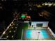 Nighttime aerial view featuring a backyard with a pool, a sport court, putting green, and outdoor lighting at 6601 E Hearn Rd, Scottsdale, AZ 85254