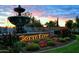 Illuminated Corte Bella community entrance with a tranquil fountain and lush landscaping set against a colorful sunset at 23034 N Pedregosa Dr, Sun City West, AZ 85375