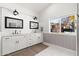 Bright bathroom featuring dual sinks, white cabinets, subway tile backsplash, and natural light from a large window at 3312 E Sells Dr, Phoenix, AZ 85018