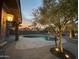 Tranquil evening view of the backyard pool, accentuated by warm lighting and mature olive trees at 1314 W Windsong Dr, Phoenix, AZ 85045