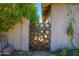 An abstract rusted metal circle gate is set between two stucco walls, next to a shaded area of greenery at 2217 N 37Th Pl, Phoenix, AZ 85008