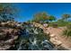 Scenic rock waterfall feature with lush vegetation and clear blue sky at 42829 N Livingstone Way, Anthem, AZ 85086