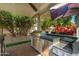 Built in stainless steel grill under a covered patio, with a television, surrounded by greenery and flowers at 5456 E Woodridge Dr, Scottsdale, AZ 85254