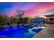 Inviting swimming pool with a rock waterfall feature, lounge chairs, and umbrellas against a colorful sky at 9183 W Foothill Dr, Peoria, AZ 85383