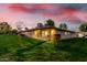 Charming home featuring a spacious backyard with lush green lawn, covered patio, and colorful sunset at 12703 W Shadow Hills Dr, Sun City West, AZ 85375
