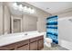 This bathroom features tile floors, vanity with a sink, toilet, and tub with a blue shower curtain at 42015 W Hillman Dr, Maricopa, AZ 85138