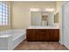 Bathroom featuring a large glass block window, a soaking tub, and wood cabinets with double sinks and a large mirror at 5032 W Yearling Rd, Phoenix, AZ 85083