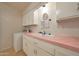 A kitchen sink area with white cabinets, laundry, and pink tile countertops at 10650 W Riviera Dr, Sun City, AZ 85351