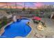 Stunning pool with a rock waterfall slide, a built-in fire pit, and an umbrella-covered patio table at sunset at 11965 W Monte Vista Rd, Avondale, AZ 85392