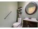 Cozy half bath features neutral green walls, dark vanity, and decorative round mirror at 15137 W Yucatan Dr, Surprise, AZ 85379