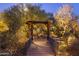 An illuminated wooden foot bridge over a rock bed covered in mulch and surrounded by desert vegetation at 25002 N Quail Haven Dr, Rio Verde, AZ 85263