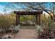 A backyard pergola has stone legs and a concrete seating area, surrounded by lush desert landscaping at 25002 N Quail Haven Dr, Rio Verde, AZ 85263