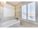 Bright bathroom featuring a bathtub with marble details, a window with white shutters, and neutral walls at 5915 E Fairfield St, Mesa, AZ 85205