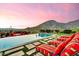 Inviting backyard pool with red striped lounge chairs overlooking scenic desert landscape with mountains and pink sky at 10935 E Grandview Way, Scottsdale, AZ 85255