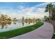 Picturesque community lake with a water fountain, lush green grass, walking path, and palm trees under a blue sky at 2511 W Queen Creek Rd # 307, Chandler, AZ 85248