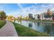 Scenic view of a community lake with a walking path, lush green grass, and residential buildings under a sunny sky at 2511 W Queen Creek Rd # 307, Chandler, AZ 85248