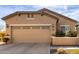 Tan stucco home with a two-car garage featuring decorative fixtures and desert landscaping at 26057 W Sequoia Dr, Buckeye, AZ 85396