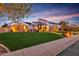 Inviting home exterior with stone accents, manicured lawn, and warm lighting, creating a welcoming ambiance in the evening at 7055 E Ivyglen Cir, Mesa, AZ 85207