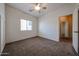 A cozy carpeted bedroom with a ceiling fan, window, and an open doorway enhancing comfort and functionality at 14616 W Ventura St, Surprise, AZ 85379