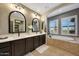 Luxurious bathroom with dual sinks, dark cabinets, a soaking tub, and bright natural light at 20785 W Canyon Dr, Buckeye, AZ 85396