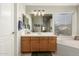 Bright bathroom featuring a vanity with natural wood cabinetry and a large mirror, plus a window over a corner tub at 1202 E Desert Broom Way, Phoenix, AZ 85048