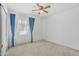 Bright bedroom featuring neutral carpet, ceiling fan, and window with blue curtains at 43556 W Colby Dr, Maricopa, AZ 85138