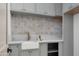 Gray laundry room featuring a white farmhouse sink and tiled backsplash, complemented by stylish cabinetry and a stone countertop at 6312 E Calle Del Paisano --, Scottsdale, AZ 85251