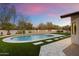 Inviting backyard pool with stone patio, lush artificial turf, desert plants, and a colorful evening sky at 8254 E Juan Tabo Rd, Scottsdale, AZ 85255