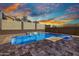 A modern pool with a soothing water feature, enhanced by elegant stone decking and dramatic sunset lighting at 11954 W Melinda Ln, Sun City, AZ 85373