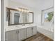 Bright bathroom boasts a double sink vanity with white cabinets, a large framed mirror and a soaking tub beneath a sunny window at 1447 S Portland Ave, Gilbert, AZ 85296