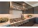 Close up view of a modern gas range stove, stainless hood, tile backsplash, and custom cabinetry in the kitchen at 24066 S 218Th Pl, Queen Creek, AZ 85142