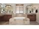 Bathroom featuring a soaking tub with travertine tile surround and double sink vanities with granite countertop at 9901 E Bahia Dr, Scottsdale, AZ 85260