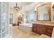 Bright primary bathroom featuring tiled flooring, soaking tub, dual vanities, and elegant chandelier lighting at 12160 E Whispering Wind Dr, Scottsdale, AZ 85255